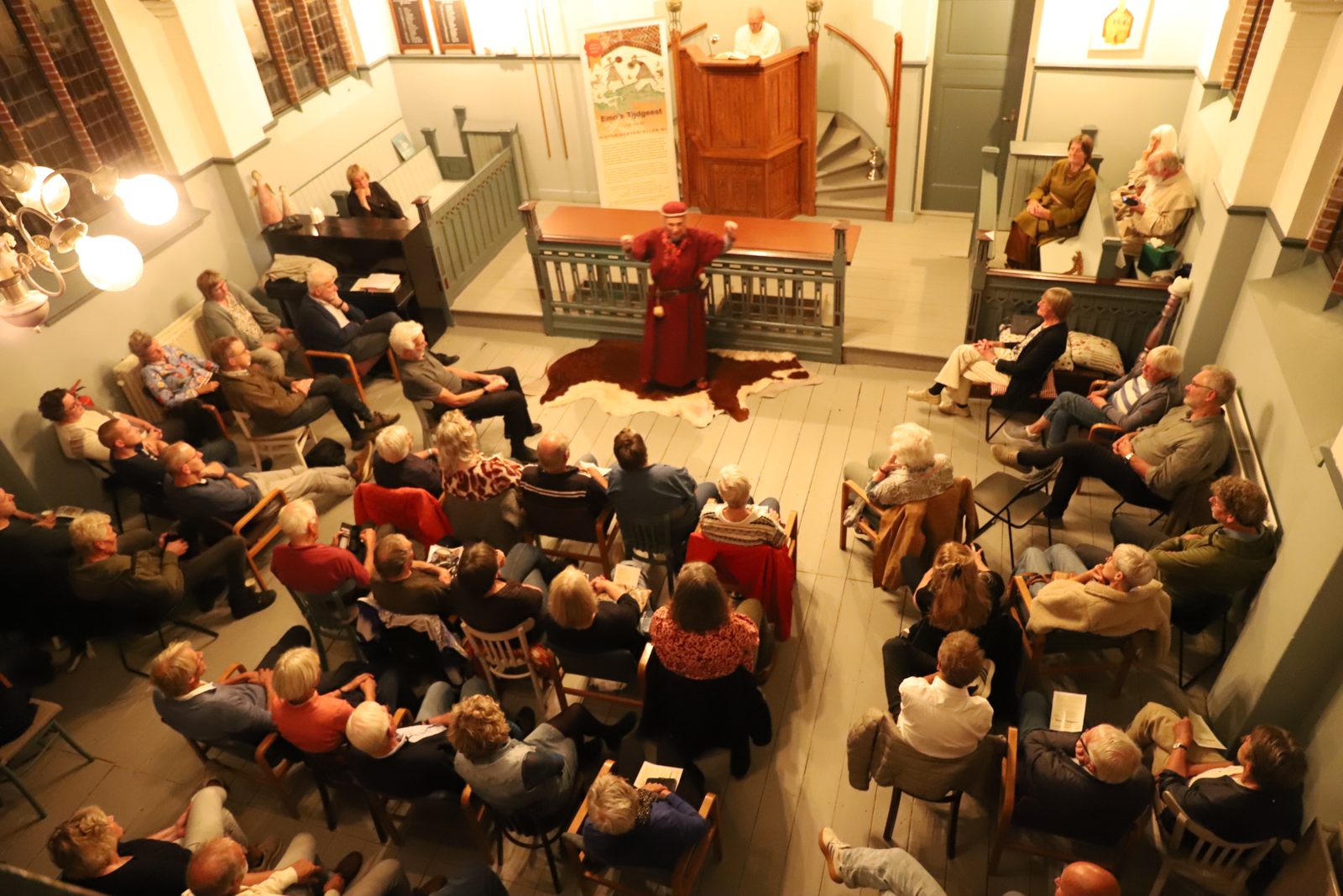 Verteller in rood kostuum voor een volle zaal in 't Oude Kerkje